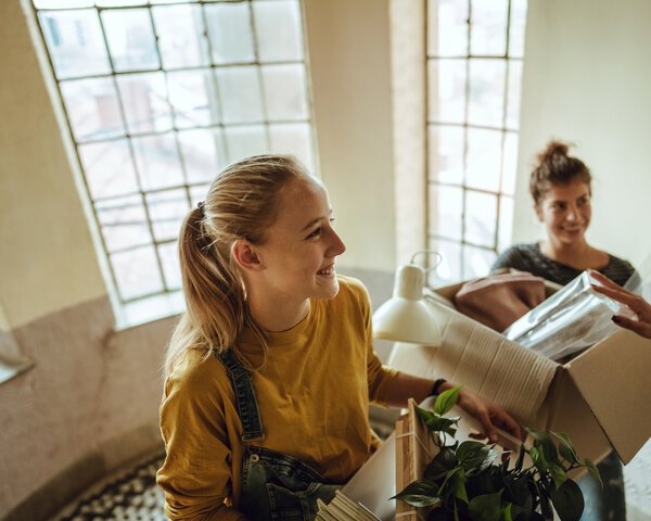 zwei Frauen/Mädchen mit Umzugskartons im Treppenhaus | © AleksandarNakic - Getty Images